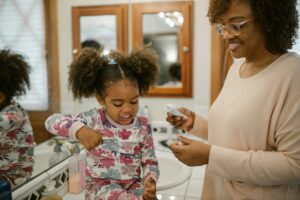 Niña cepillando sus dientes con su mamá