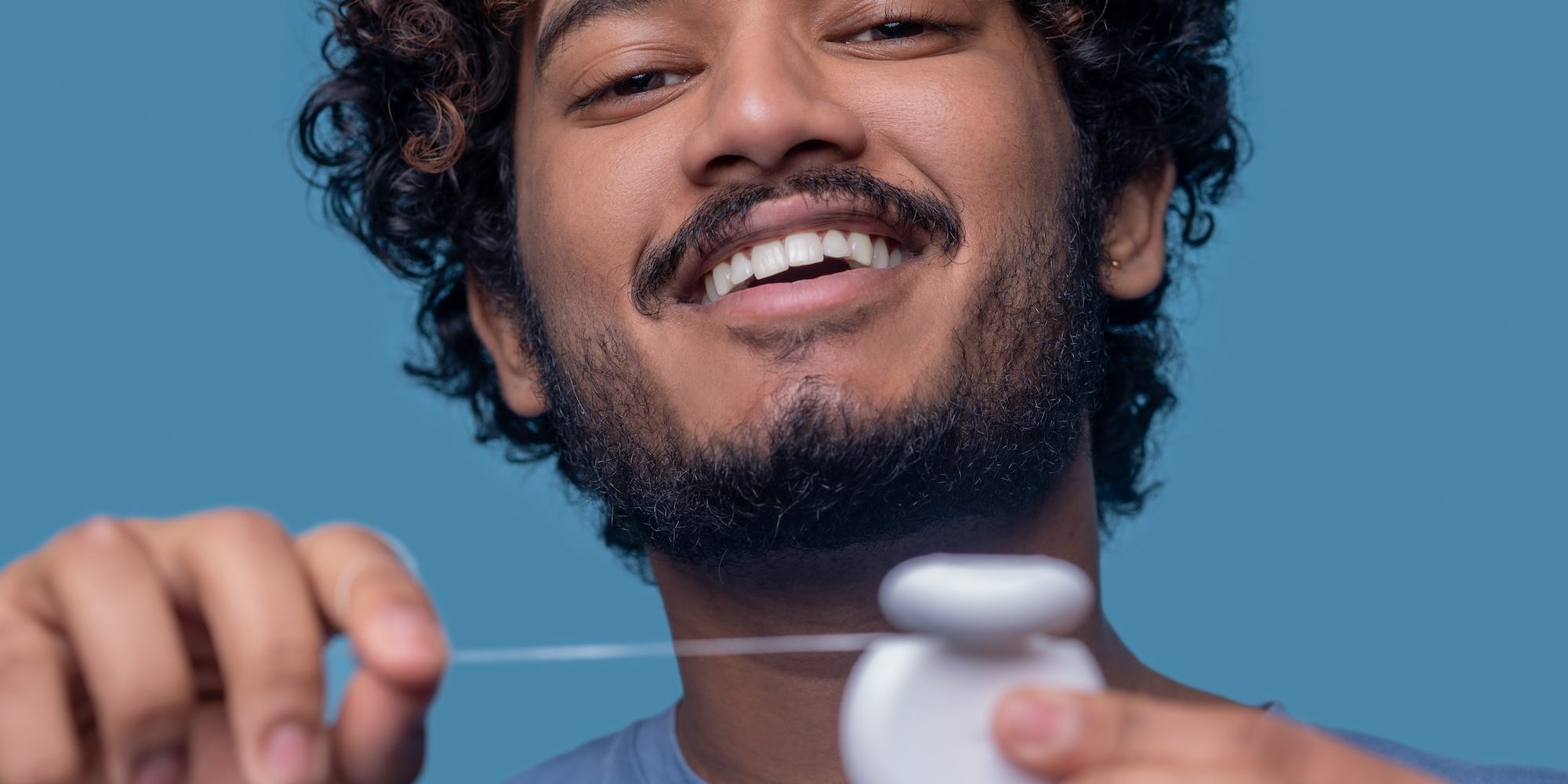 closeup-portrait-of-cheerful-indian-guy-holding-the-open-dental-floss-container-in-his-hands closeup-portrait-of-cheerful-indian-guy-holding-the-open-dental-floss-container-in-his-hands