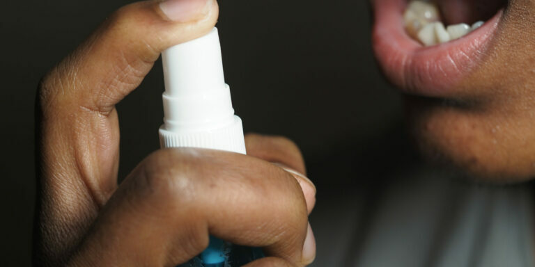 A person applies a refreshing spray into the mouth for hygiene.
